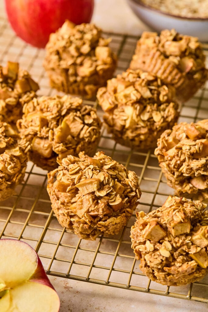 Oatmeal apple muffins on a wire cooling rack. In front of the rack is half a cut apple.