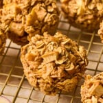 Apple oatmeal muffins on a wire cooling rack. In front of the rack is an apple cut in half.