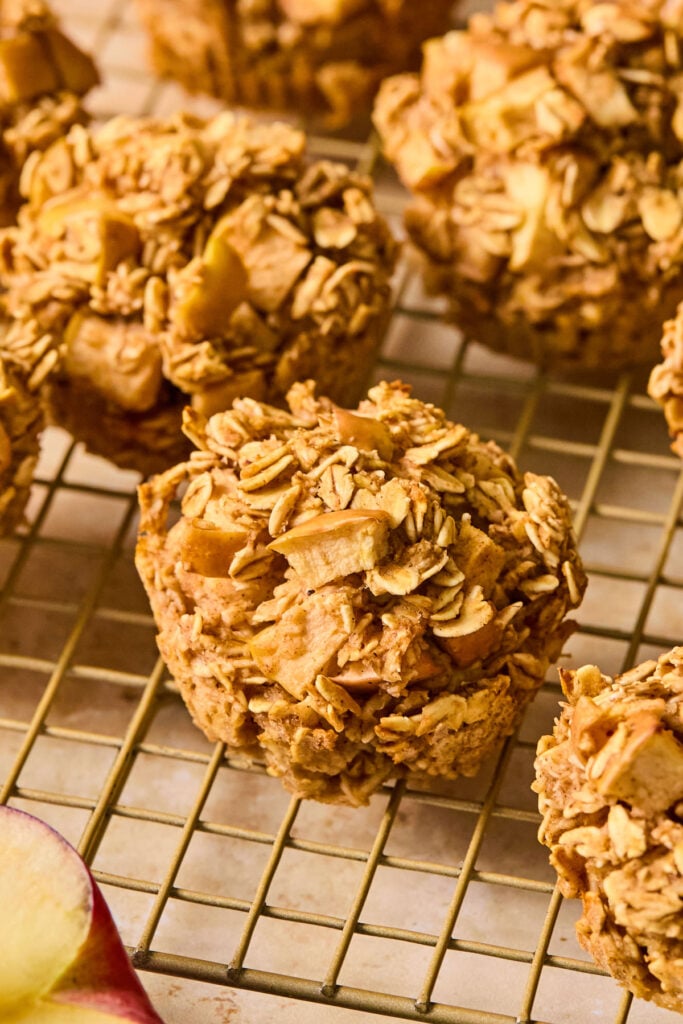 Apple oatmeal muffins on a wire cooling rack. In front of the rack is an apple cut in half.