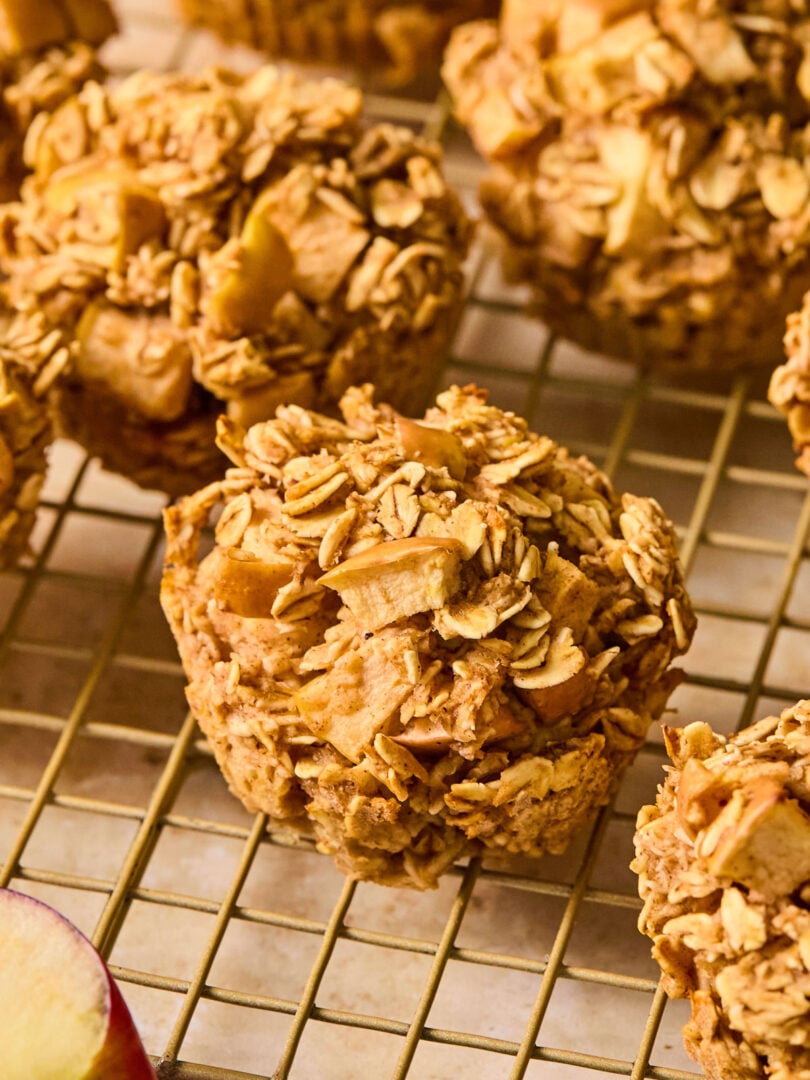 Apple oatmeal muffins on a wire cooling rack. In front of the rack is an apple cut in half.