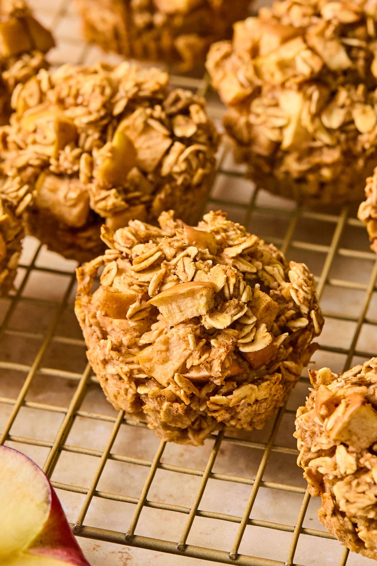 Apple oatmeal muffins on a wire cooling rack. In front of the rack is an apple cut in half.