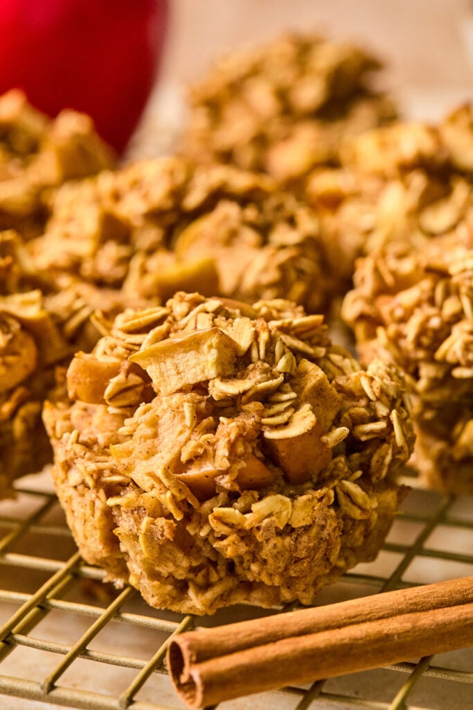 Apple oat muffins with cinnamon on a wire cooling rack. Around the muffins are a cinnamon stick and an apple.