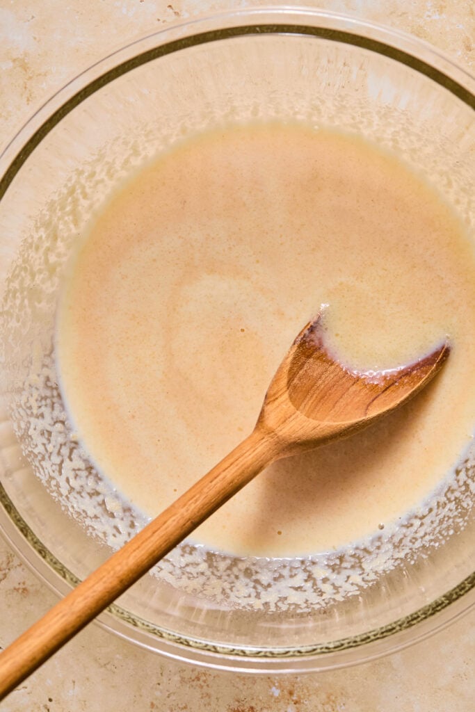 Glass mixing bowl with a wet batter with a wooden spoon in it.