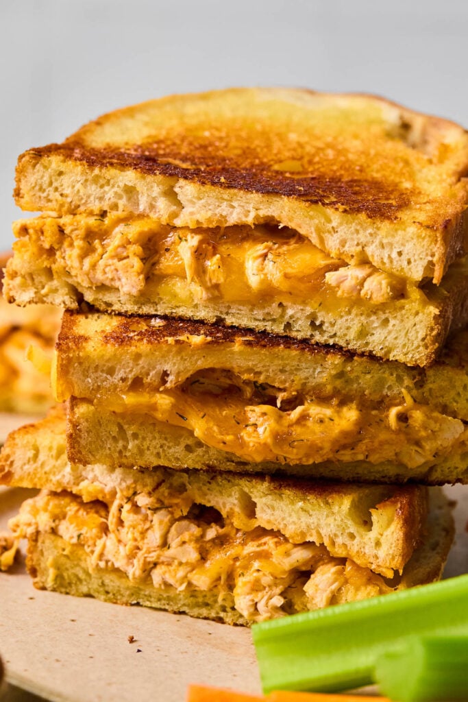Three halves of a buffalo chicken grilled cheese sandwich stacked on top of each other on a plate with some celery sticks.