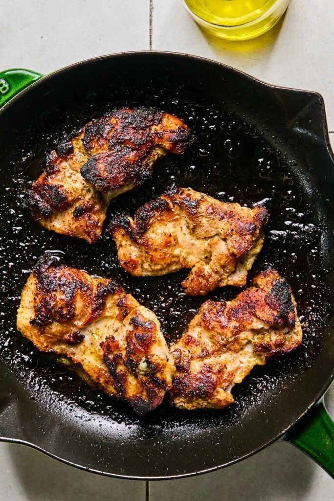 Seasoned cooked chicken thighs in a cast iron skillet.