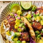 Salmon tacos on a plate with shredded cabbage, mango avocado salsa, and fish taco sauce on corn tortillas.