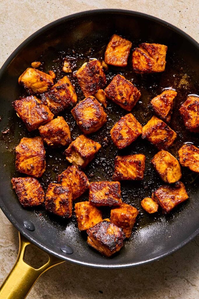 Blackened salmon cubes in a skillet.