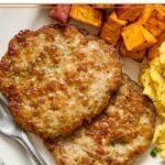A close-up of a plate with two chicken breakfast sausage patties, roasted sweet potatoes, and scrambled eggs with a fork on it.