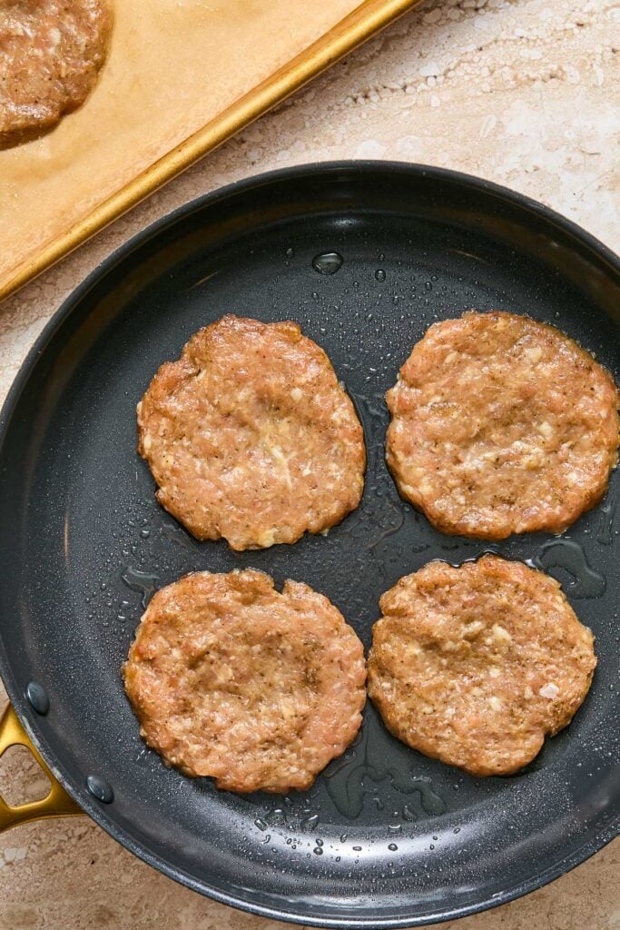 Skillet with four chicken patties being cooked.