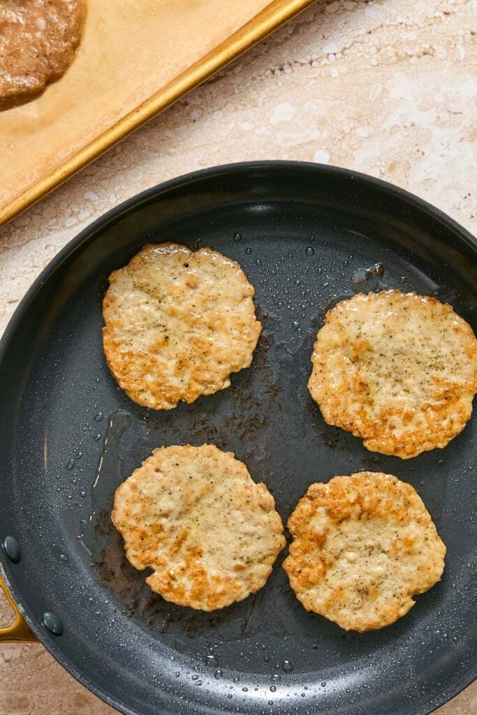 Chicken sausage patties cooking in a skillet.