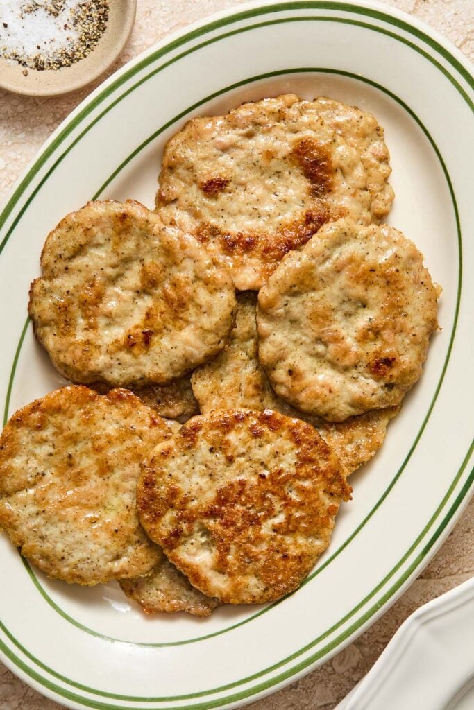 An overhead shot of a plate of breakfast chicken sausage patties. Next to the plate is a small bowl of salt and pepper.