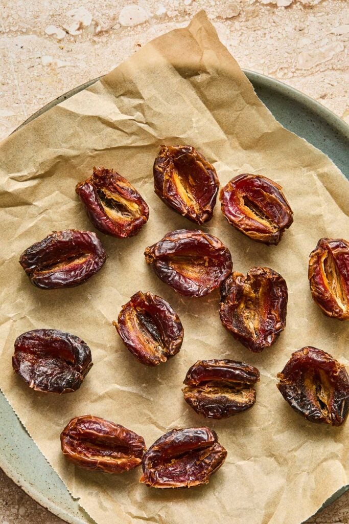 A parchment paper lined plate with a bunch of medjool dates that have been pitted and opened up.