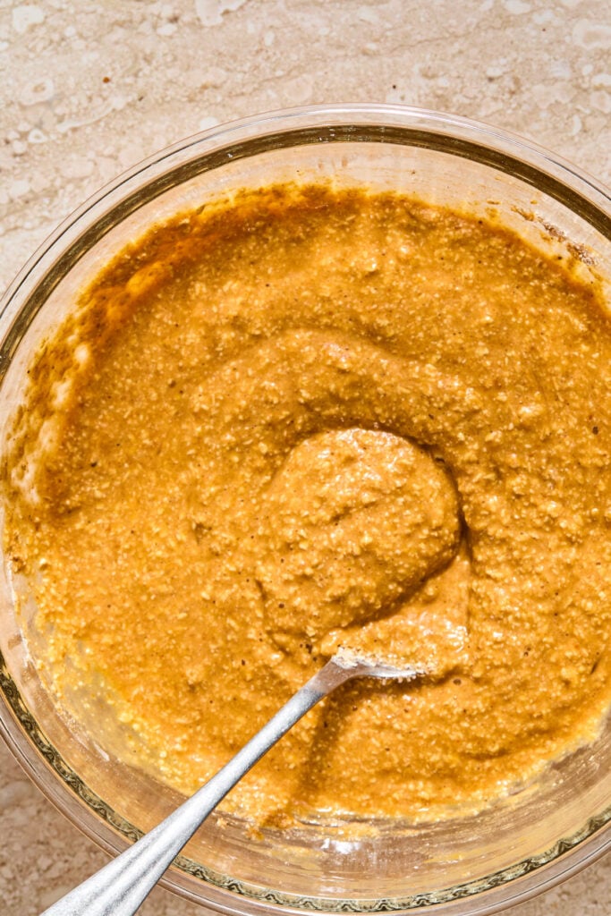 A bowl with a wet batter with a spoon in it.